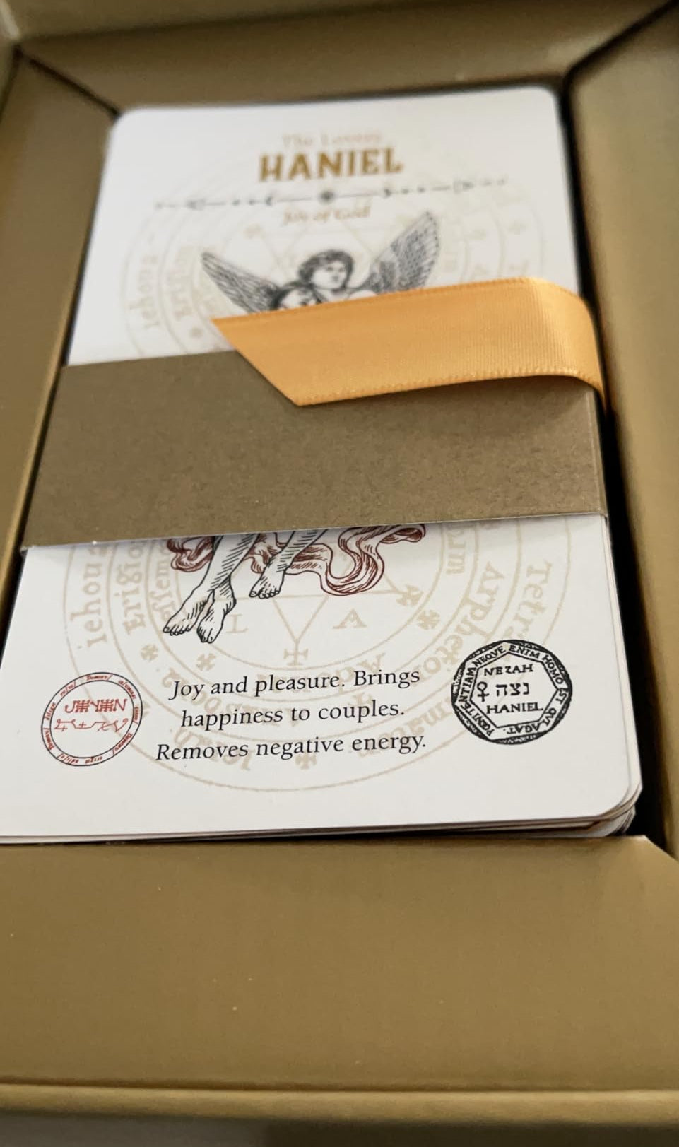 Product packaging with a card featuring the Aangel 'HANIEL' and decorative elements.